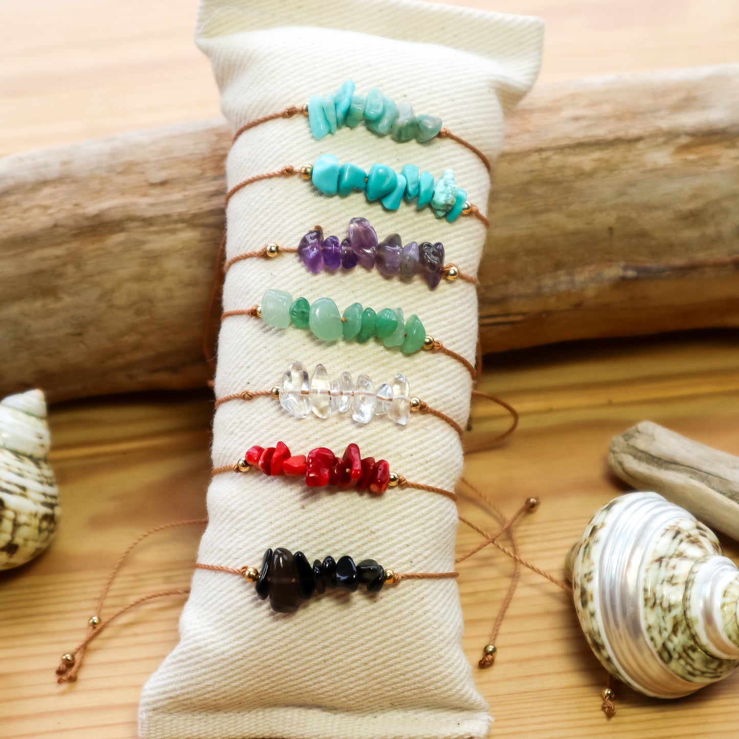 Set of colorful beaded bracelets on a white fabric with seashells and driftwood in the background.