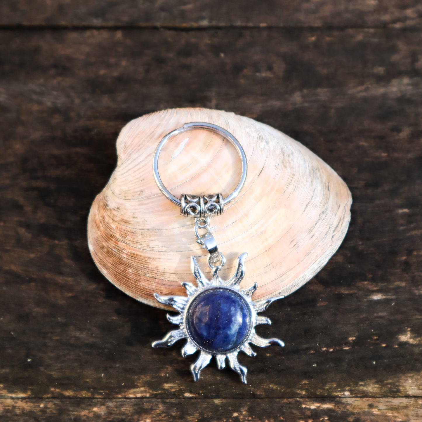 Keychain with sun design and blue stone on a shell against a wooden background