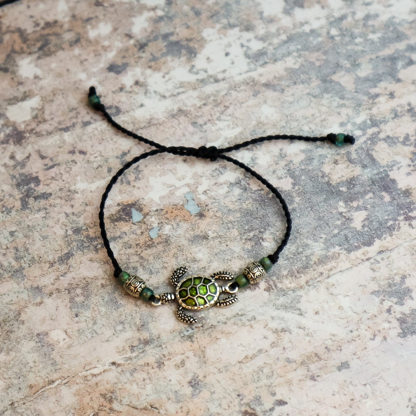 Tortoise shell bracelet with green beads on a stone surface