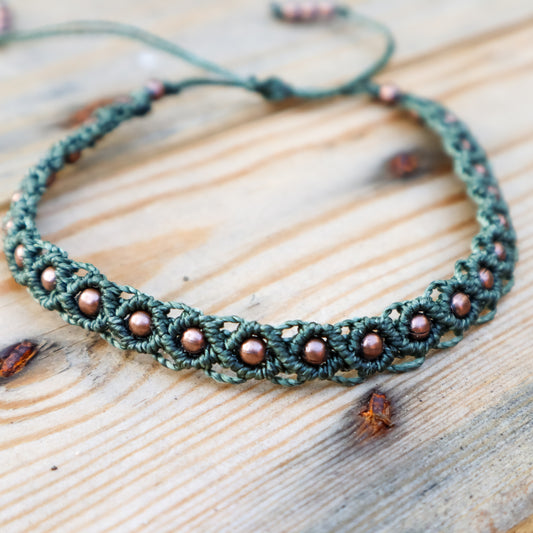 Green macrame ankle bracelet with brown beads on a wooden surface