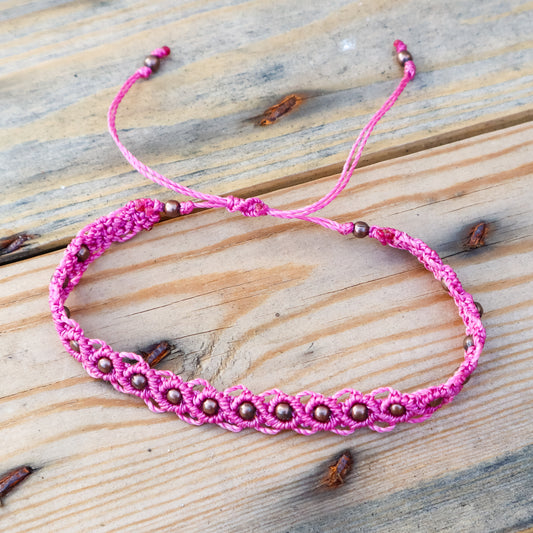 Pink macrame ankle bracelet with bronze beads on a wooden surface