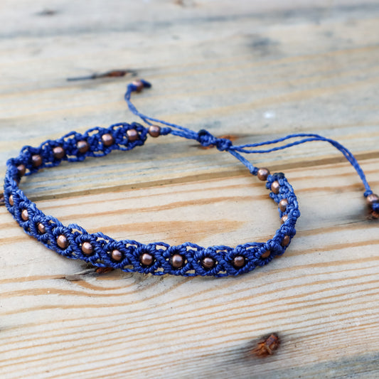 Blue macrame ankle bracelet with copper beads on a wooden surface