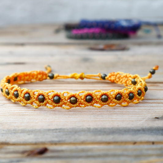 Yellow macrame ankle bracelet with bronze beads on a wooden surface