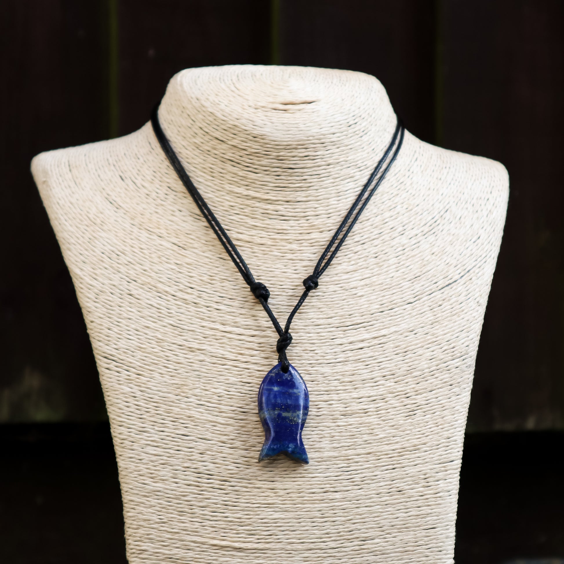 Blue fish-shaped pendant on a black cord displayed on a mannequin bust.