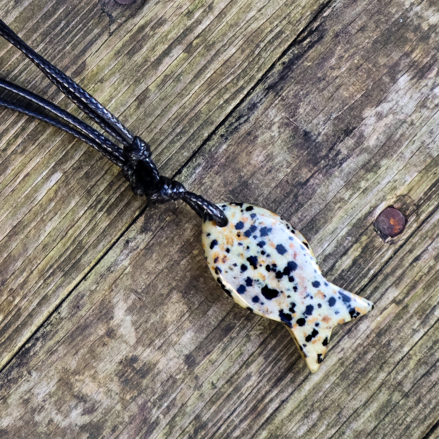 Dalmatian Jasper fish pendant on a black cord against a wooden background