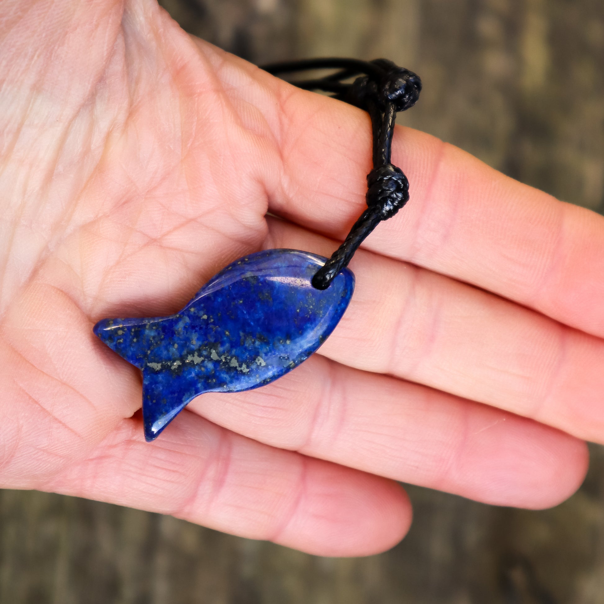 Hand holding a blue fish-shaped pendant with a black cord