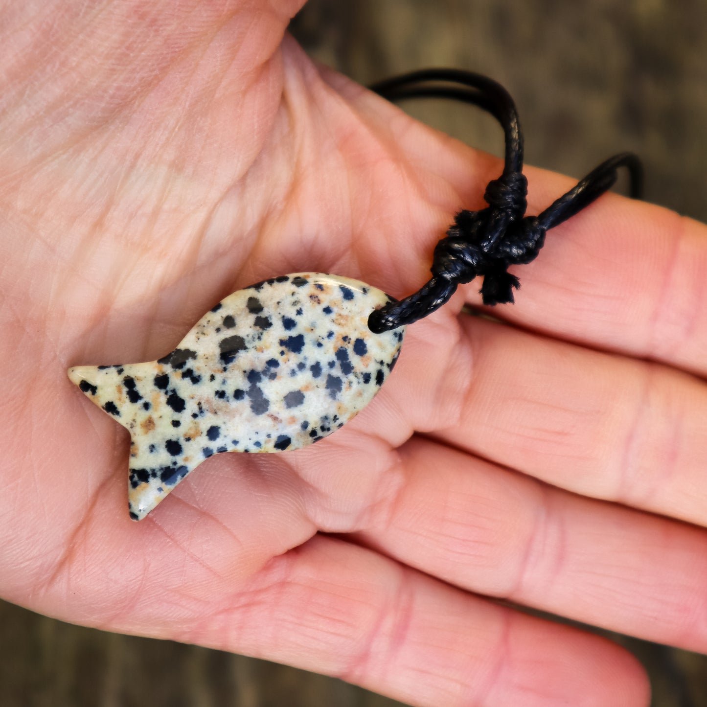 Hand holding a spotted stone pendant on a black cord