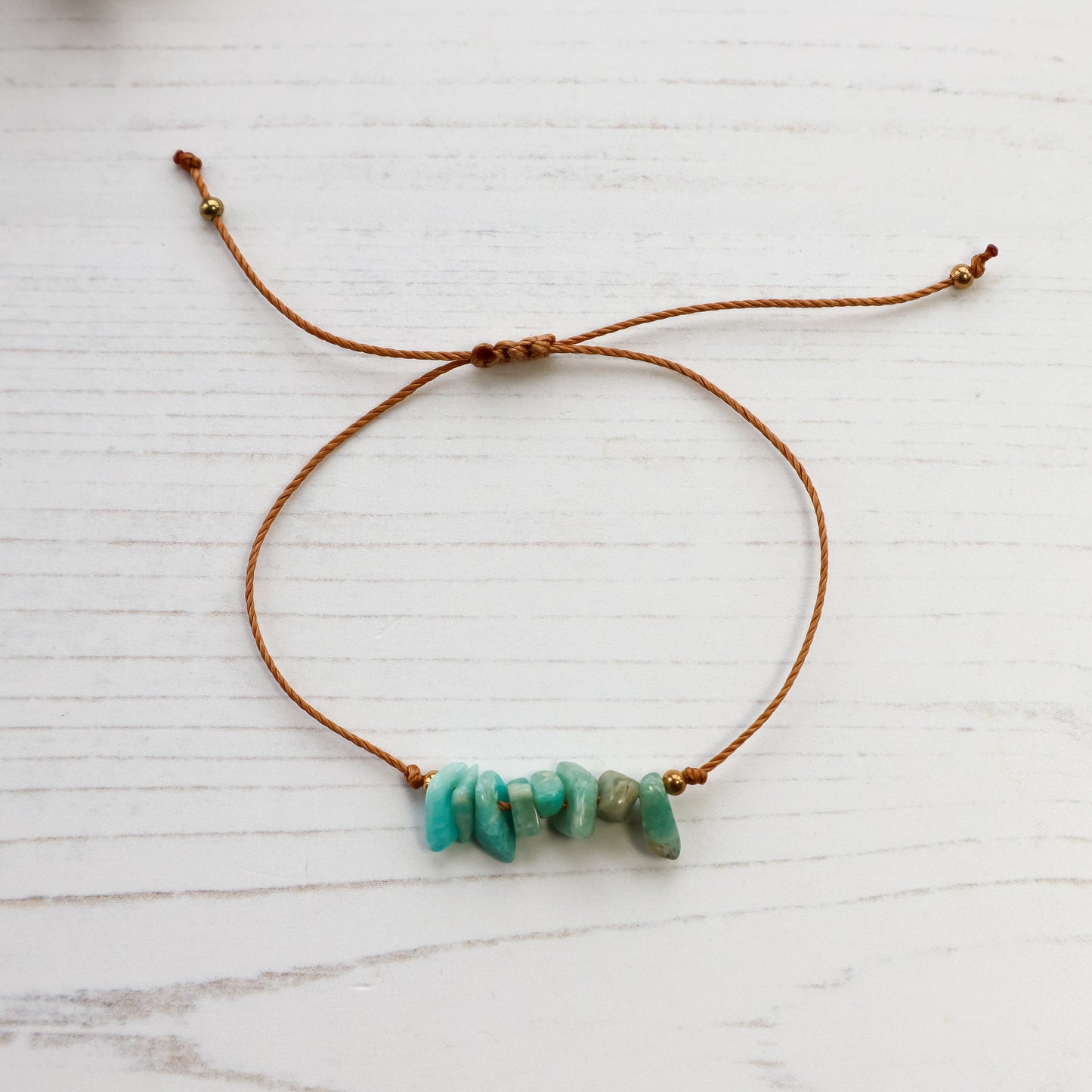 Amazonite chip bracelet with brown cord and golden beads on white wood background 