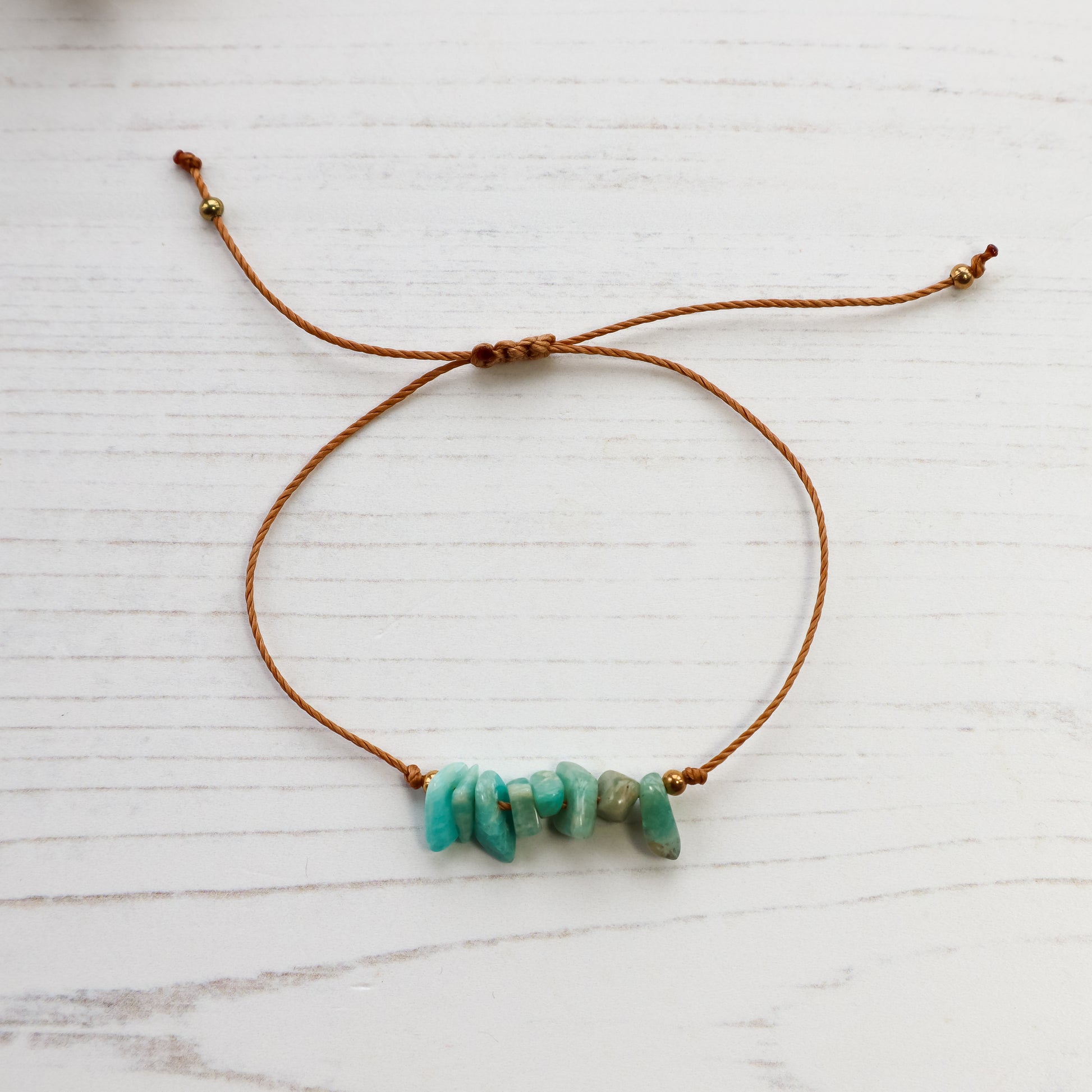 Amazonite chip bracelet with brown cord and golden beads on white wood background 