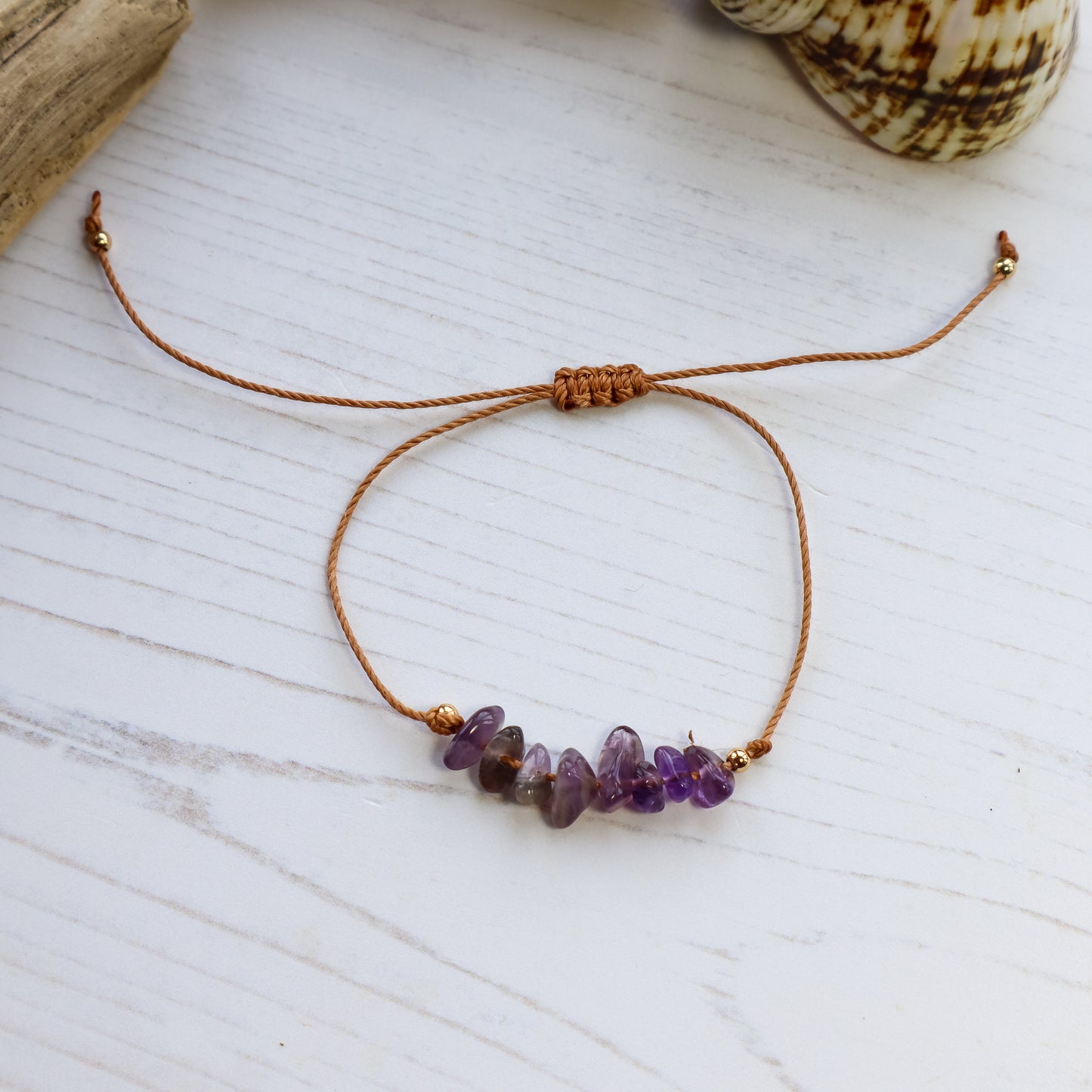 Bracelet with purple amethyst chips on white wooden background with shells and driftwood
