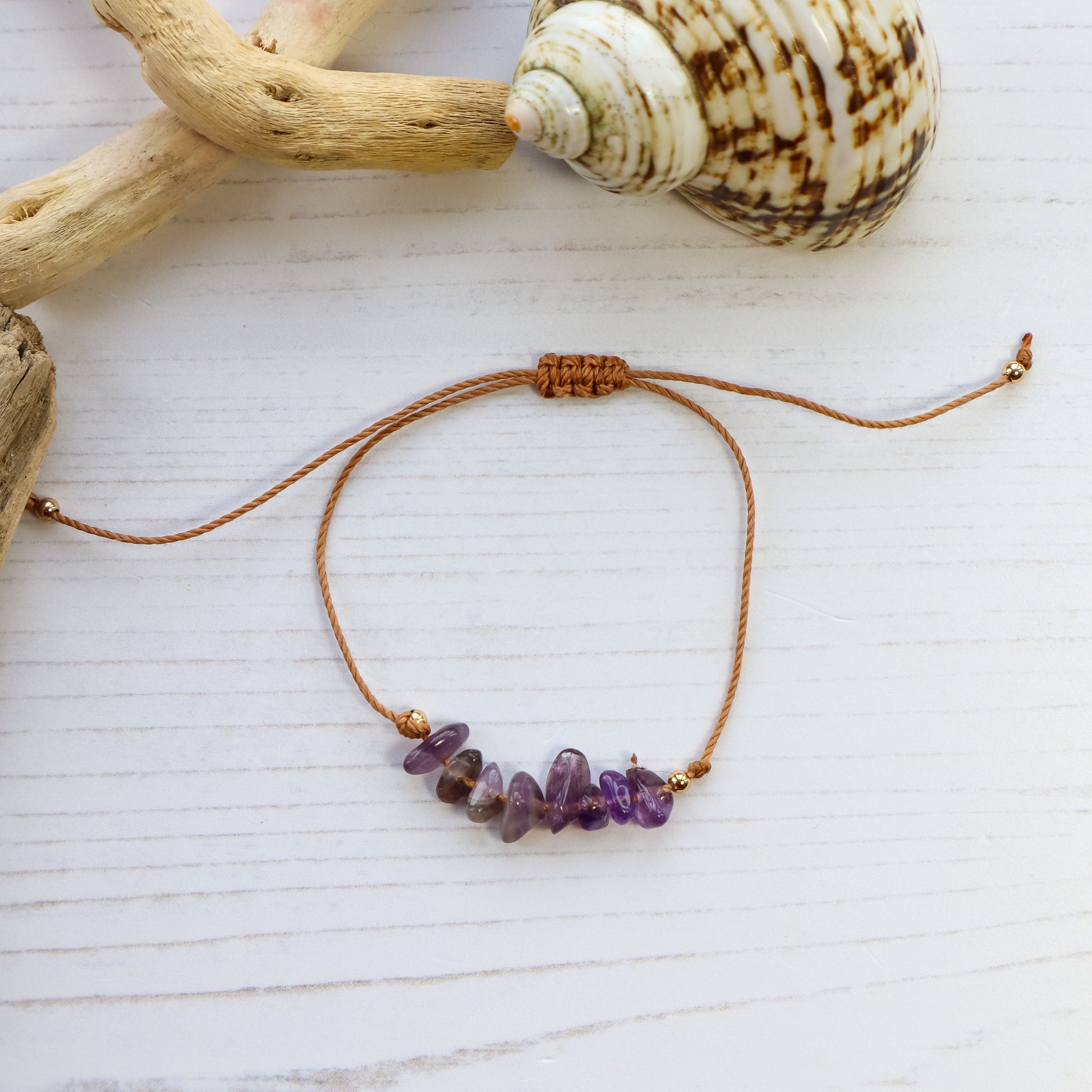 Bird's eye view of bracelet with purple amethyst chips on white wooden background with shells and driftwood