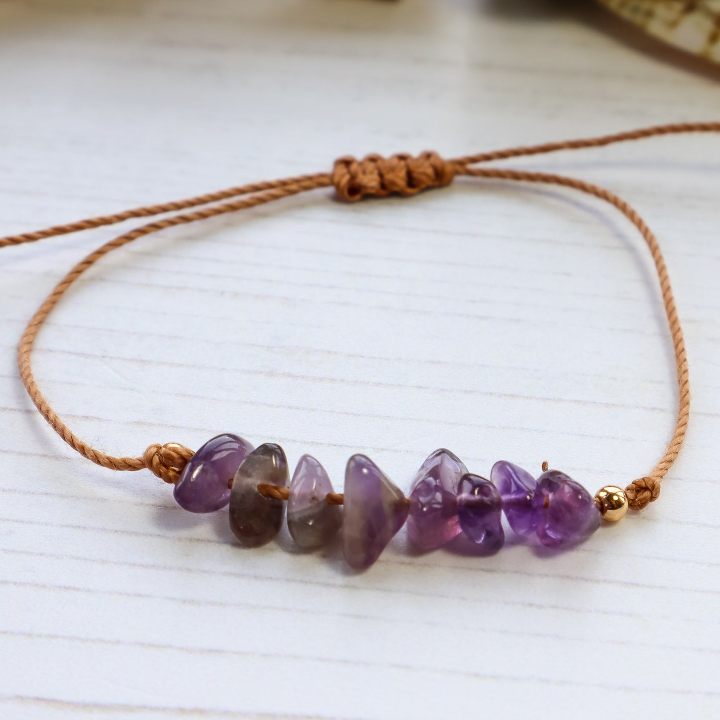 purple chip amethyst bracelet on brown cord on white background 