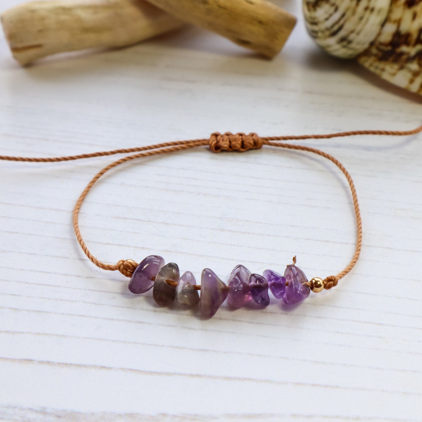Bracelet with purple amethyst chips on white wooden background with shells and driftwood