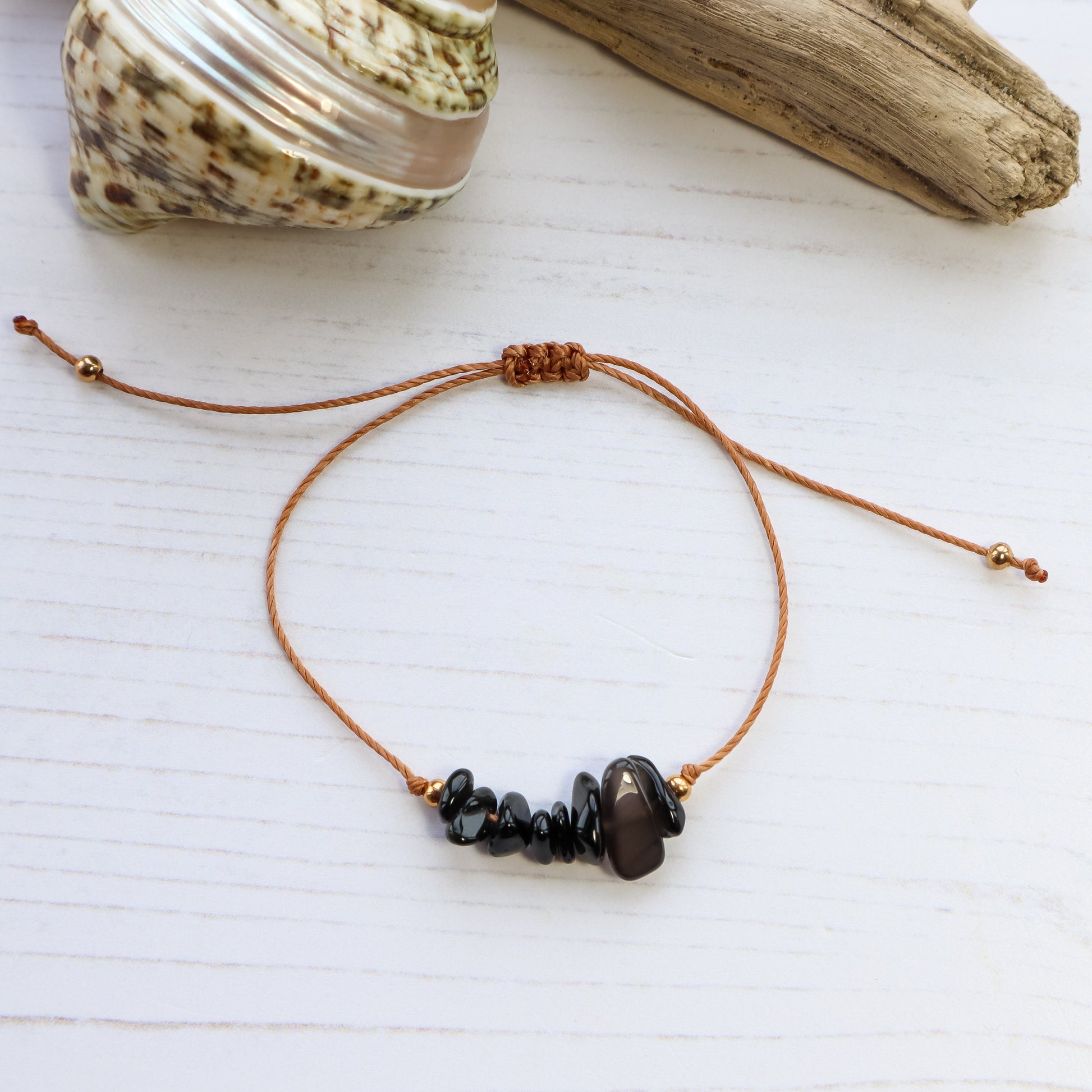 Bracelet with black chip crystals on white wooden background with shells and driftwood from above