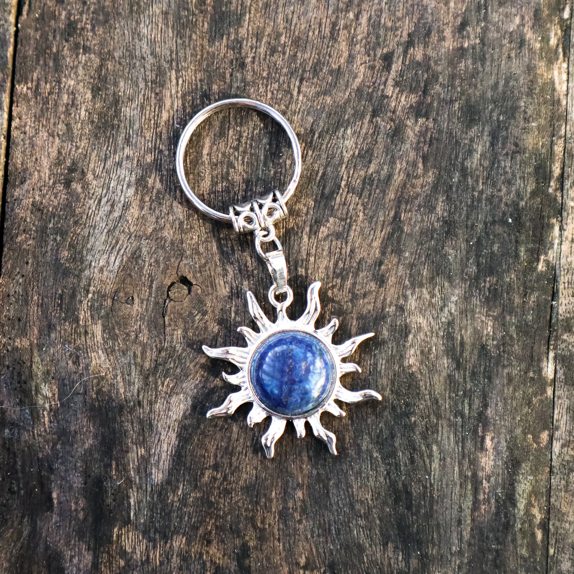 Silver keychain with sun design and blue stone on a wooden surface