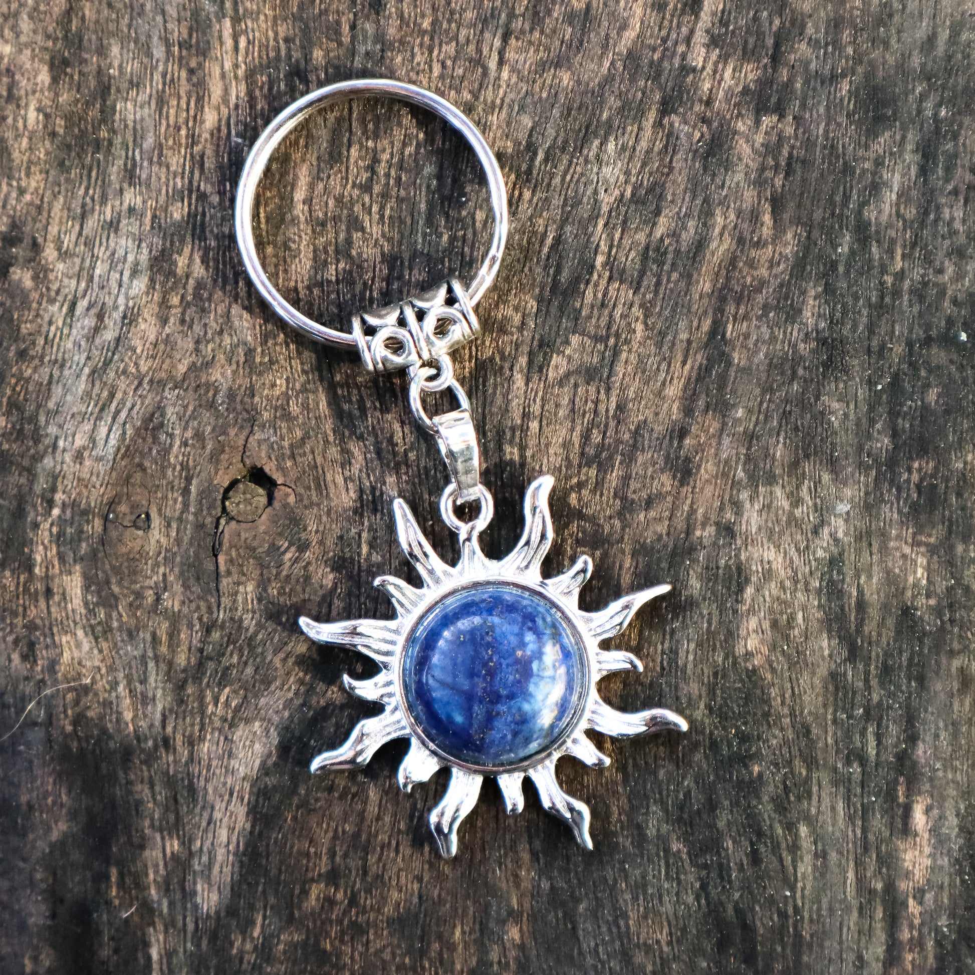 Silver sun-shaped keychain with a blue stone on a wooden surface