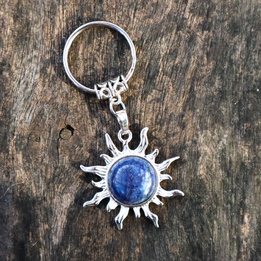 Silver sun-shaped keychain with a blue stone on a wooden surface