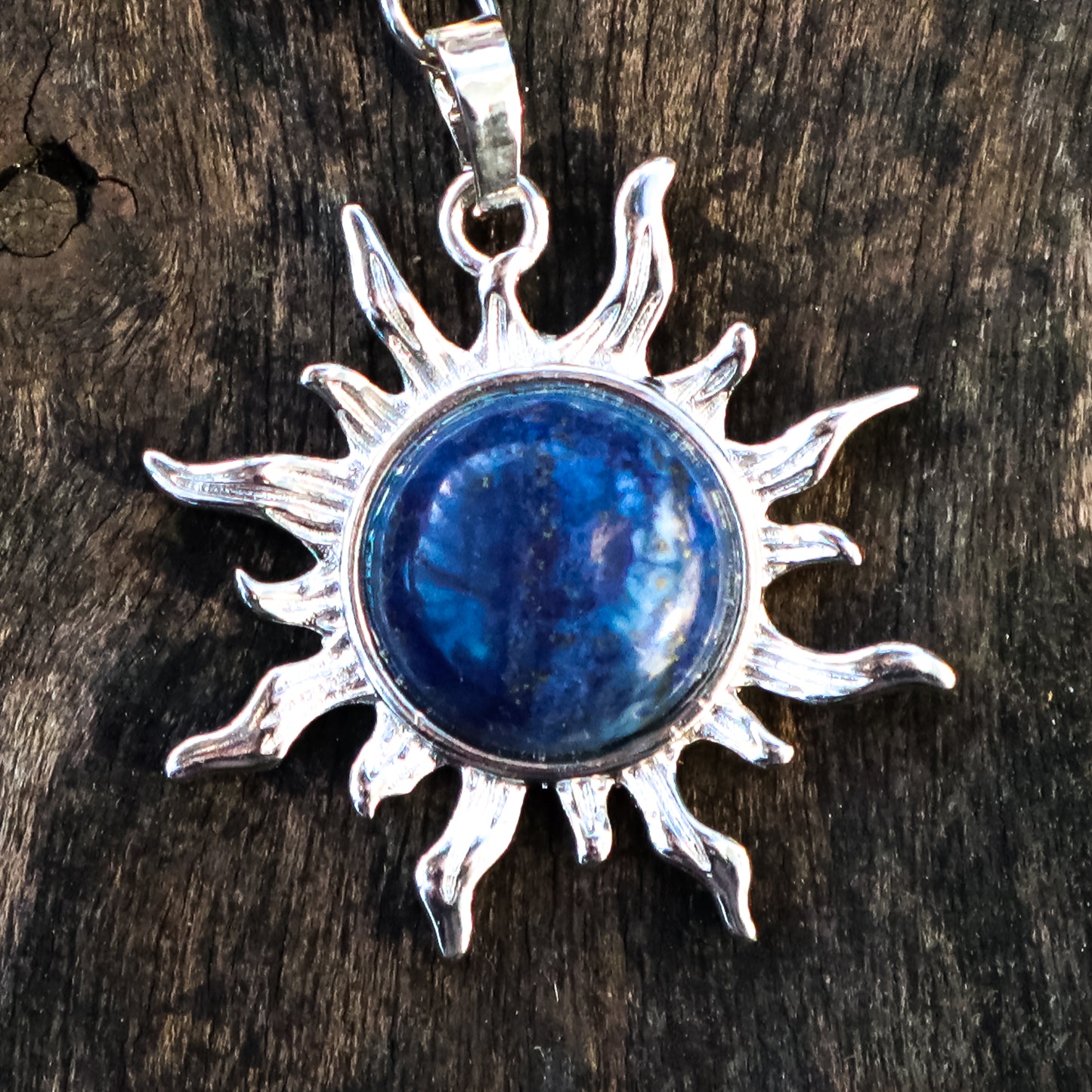 Silver sun-shaped pendant with a blue stone on a wooden surface