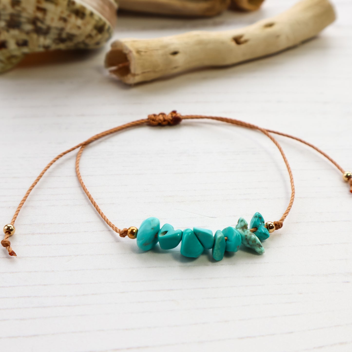 Blue chips threaded on bracelet on white wooden background with shells and driftwood