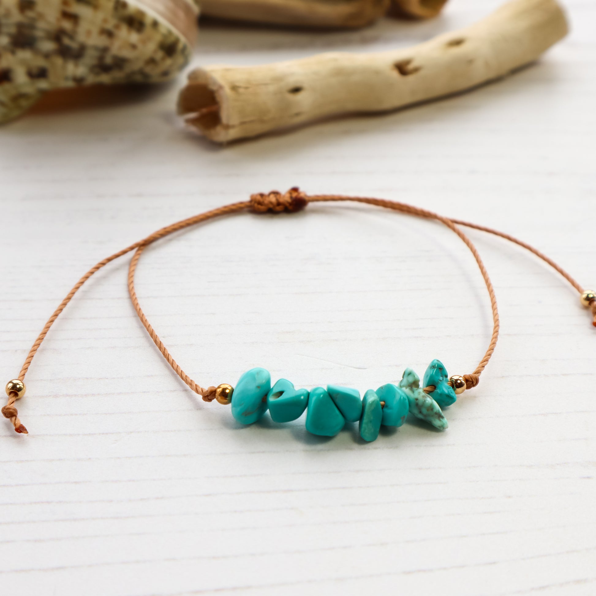 Blue chips threaded on bracelet on white wooden background with shells and driftwood