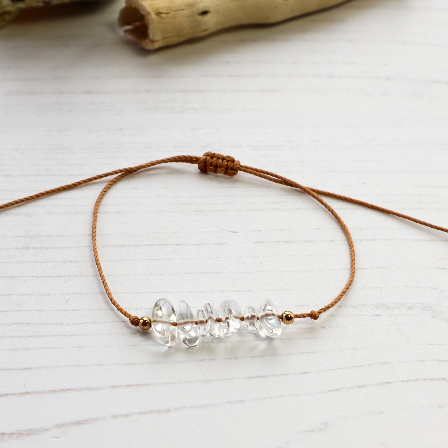 Clear quartz chip bracelet on brown cord white background with driftwood