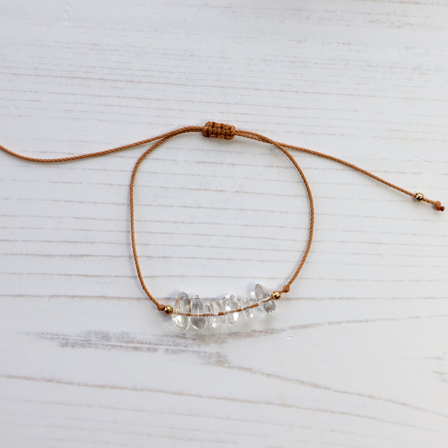 Clear quartz chip bracelet on brown cord white background 