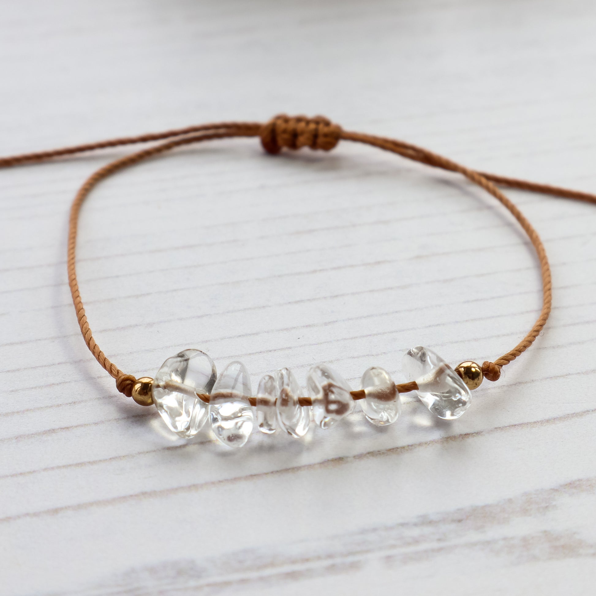 Clear quartz chip bracelet on brown cord white background 