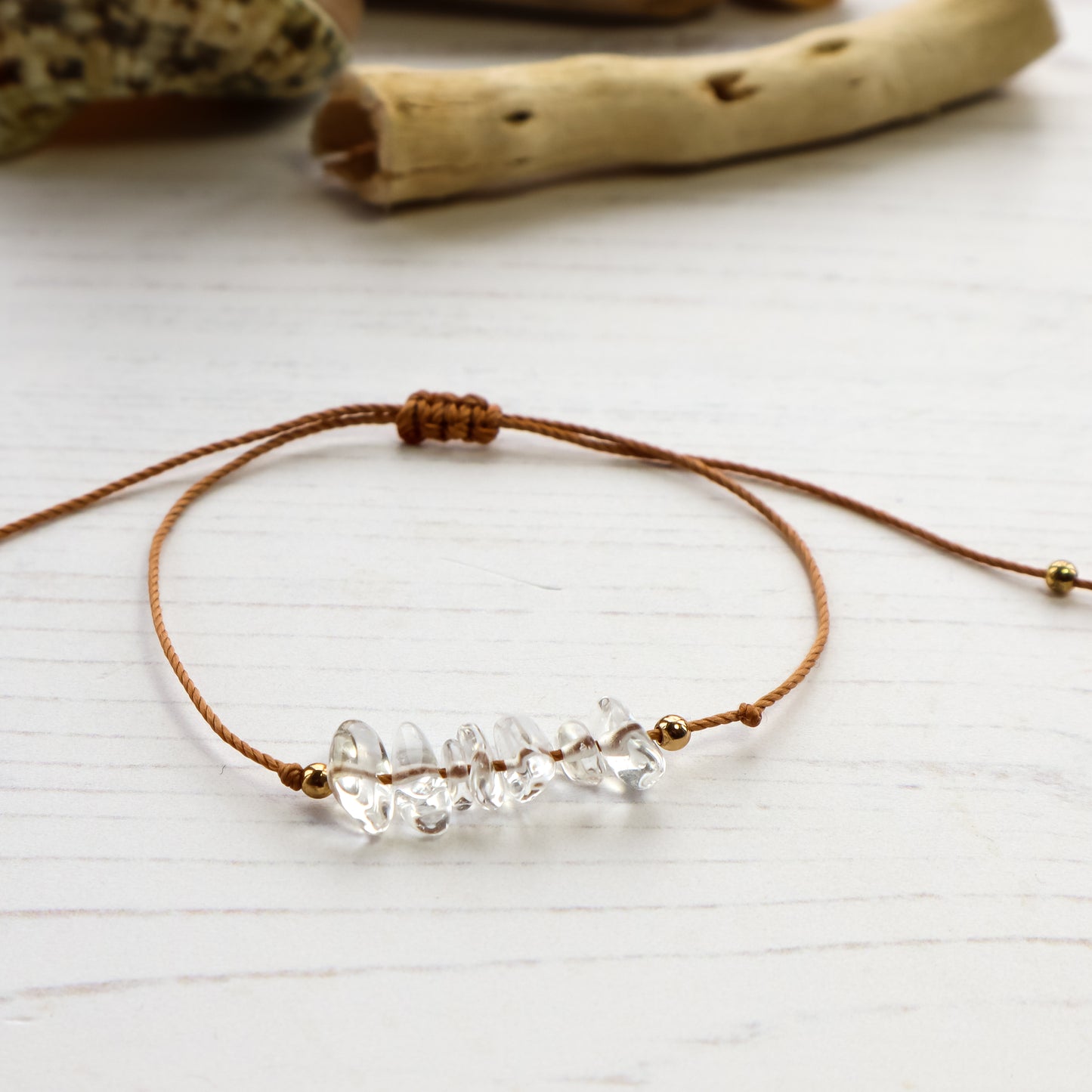 Clear quartz chip bracelet on brown cord white background with driftwood