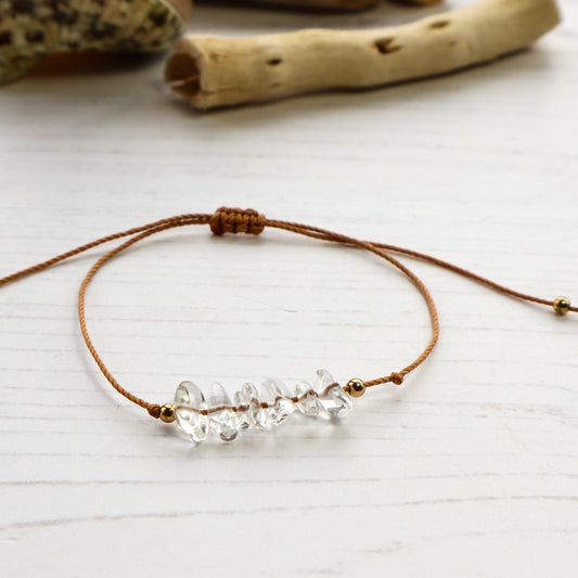 Clear quartz chip bracelet on brown cord white background with driftwood