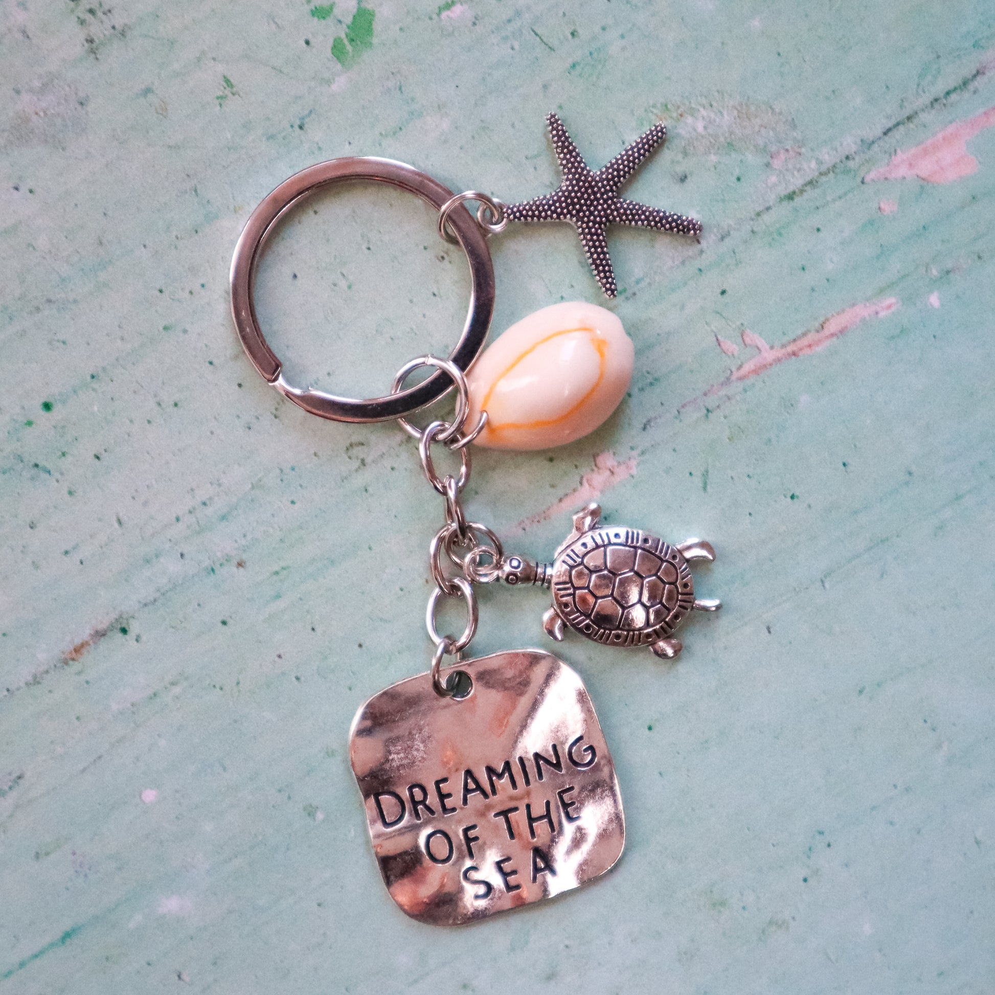 Keychain with turtle, shell, and starfish charm on a textured light blue background