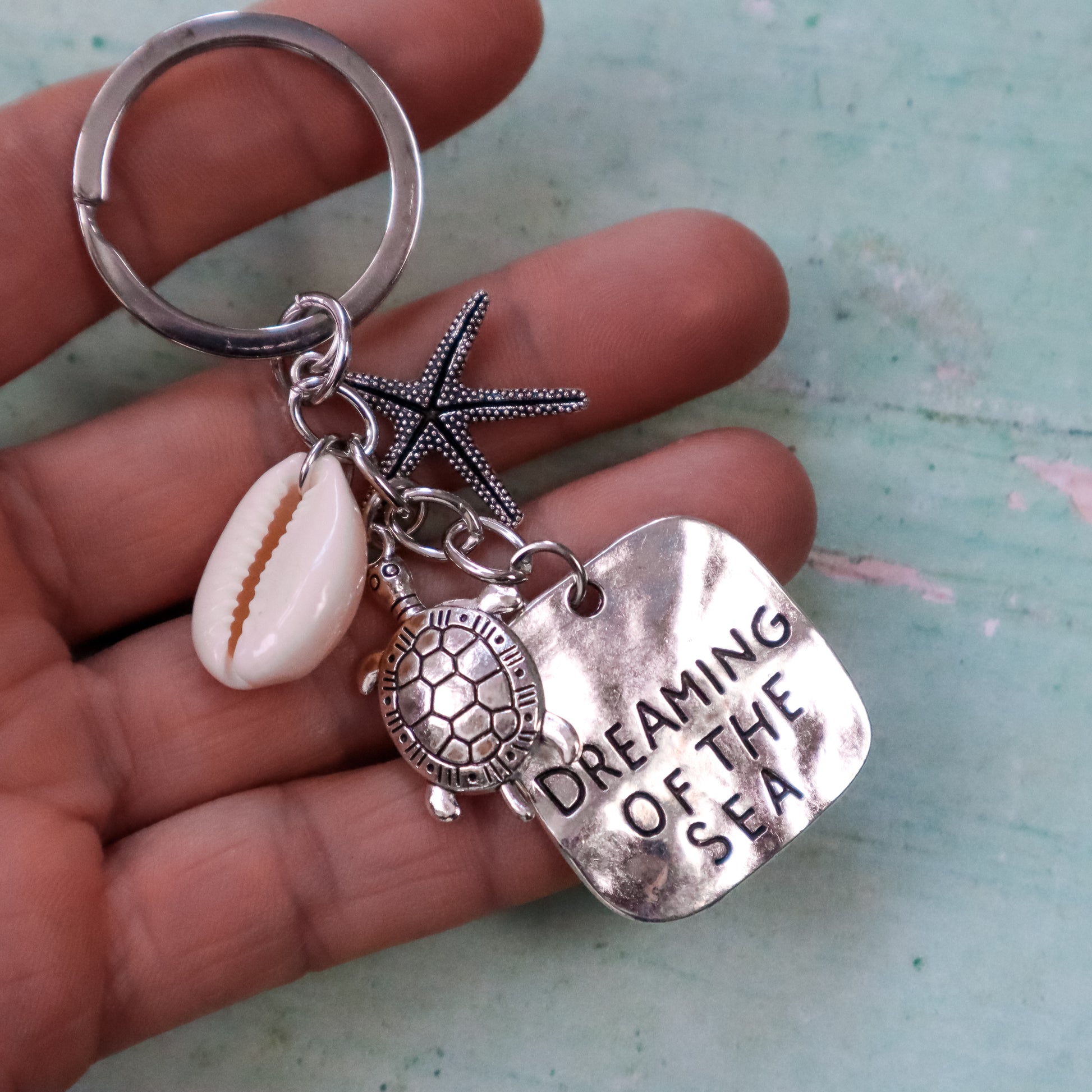 Keychain with starfish, shell, turtle charm, and 'Dreaming of the Sea' tag held in hand.