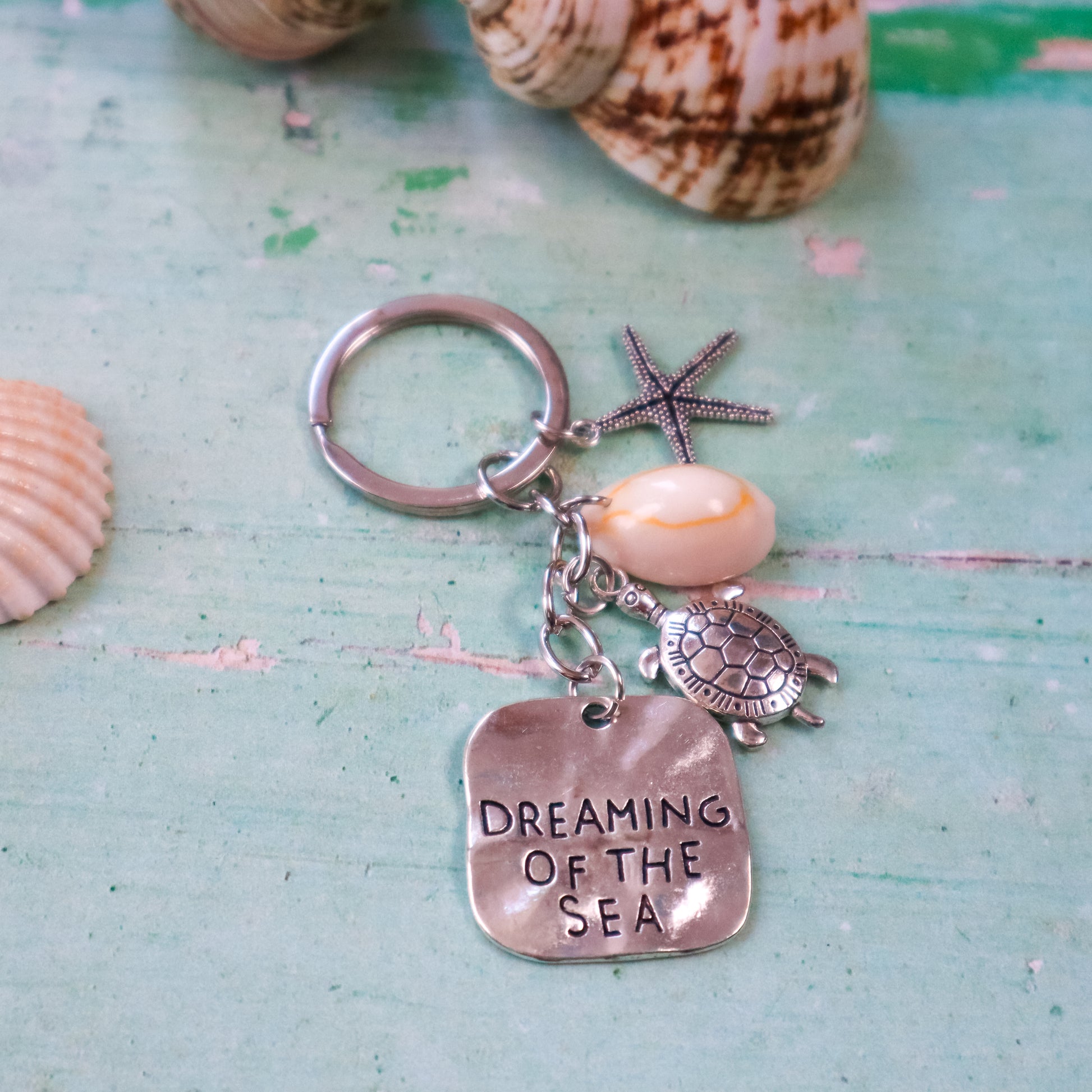 Keychain with turtle, starfish, and shell charms on a textured surface with seashells.