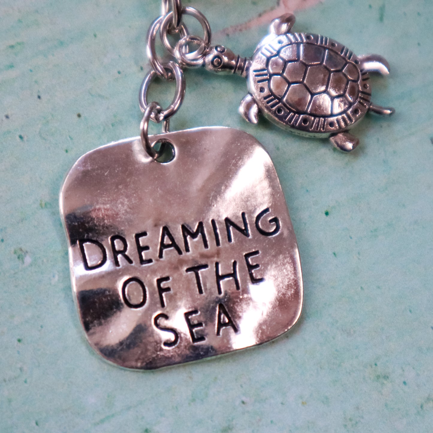 Silver keychain with turtle charm and 'Dreaming of the Sea' tag on a light blue background