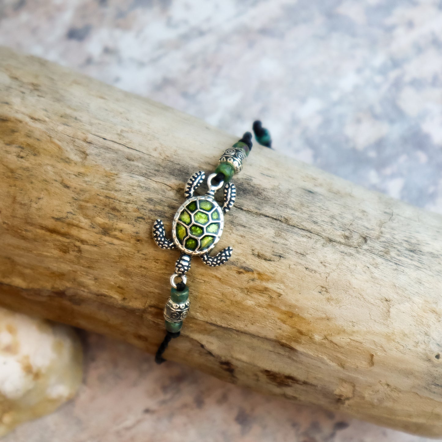 Tortoise-shaped bracelet with green accents on a wooden log