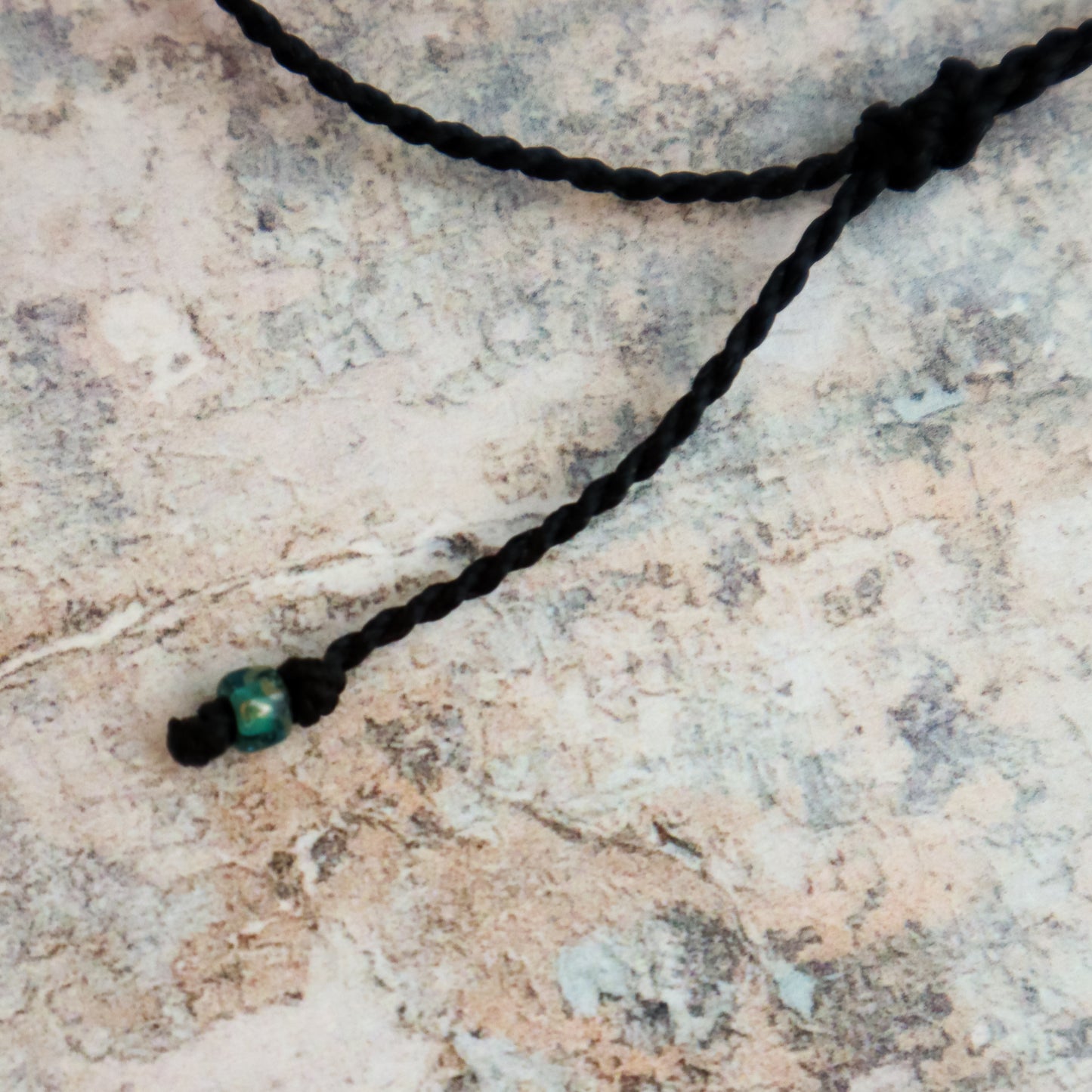Black cord with a green bead on a textured stone surface