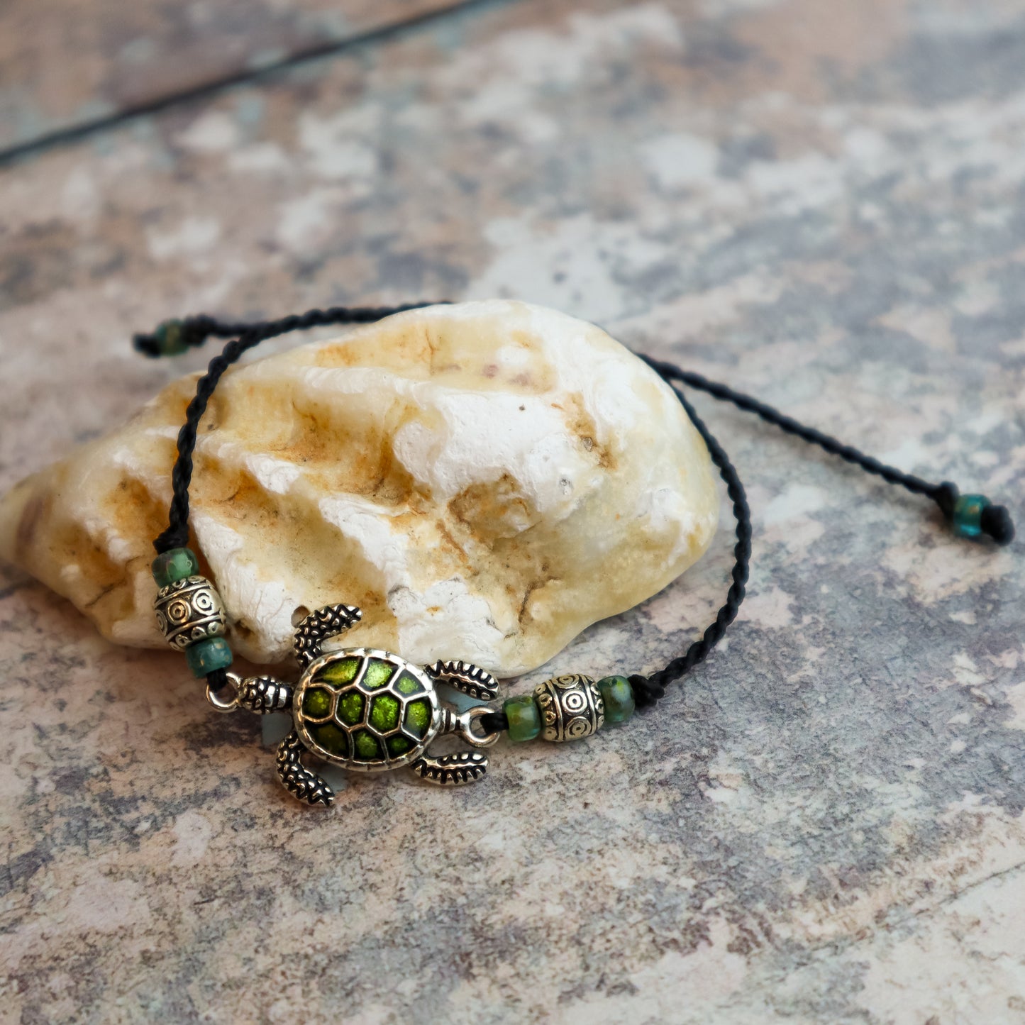Bracelet with turtle charm and green beads on a stone surface