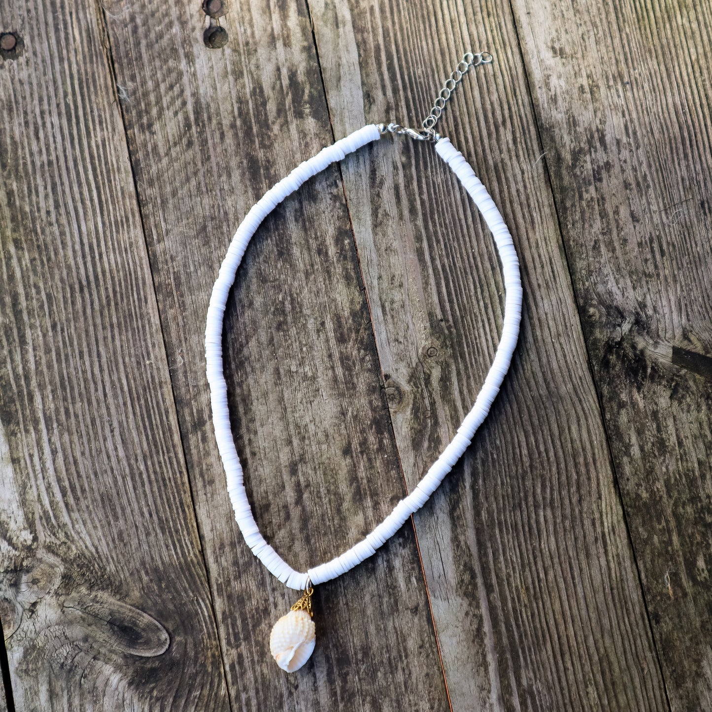 White heishi beads necklace with a small shell pendant on a wooden surface