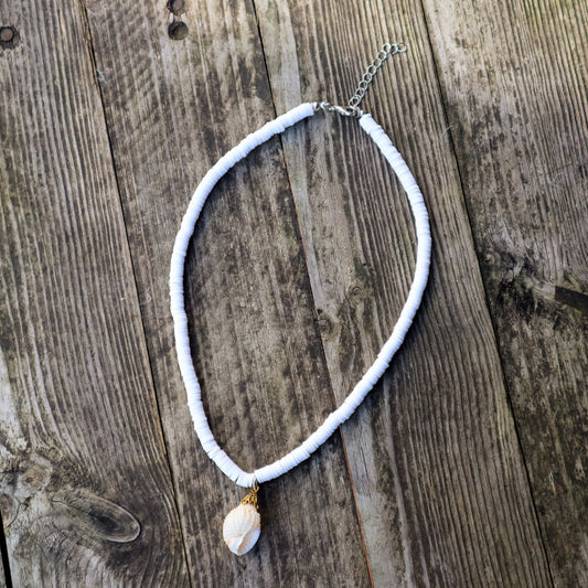White heishi beads necklace with a small shell pendant on a wooden surface