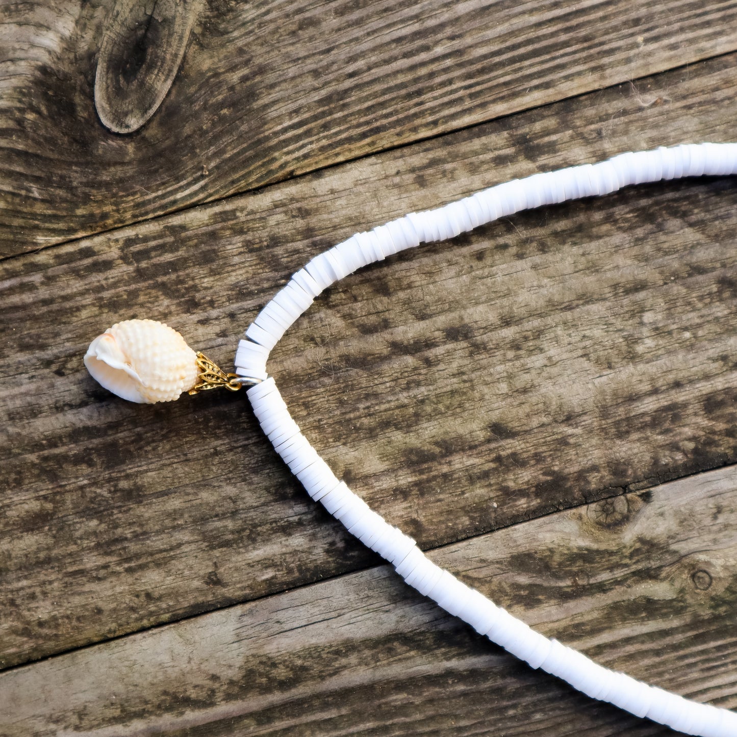 Necklace with a white beaded chain and a large stone pendant on a wooden surface
