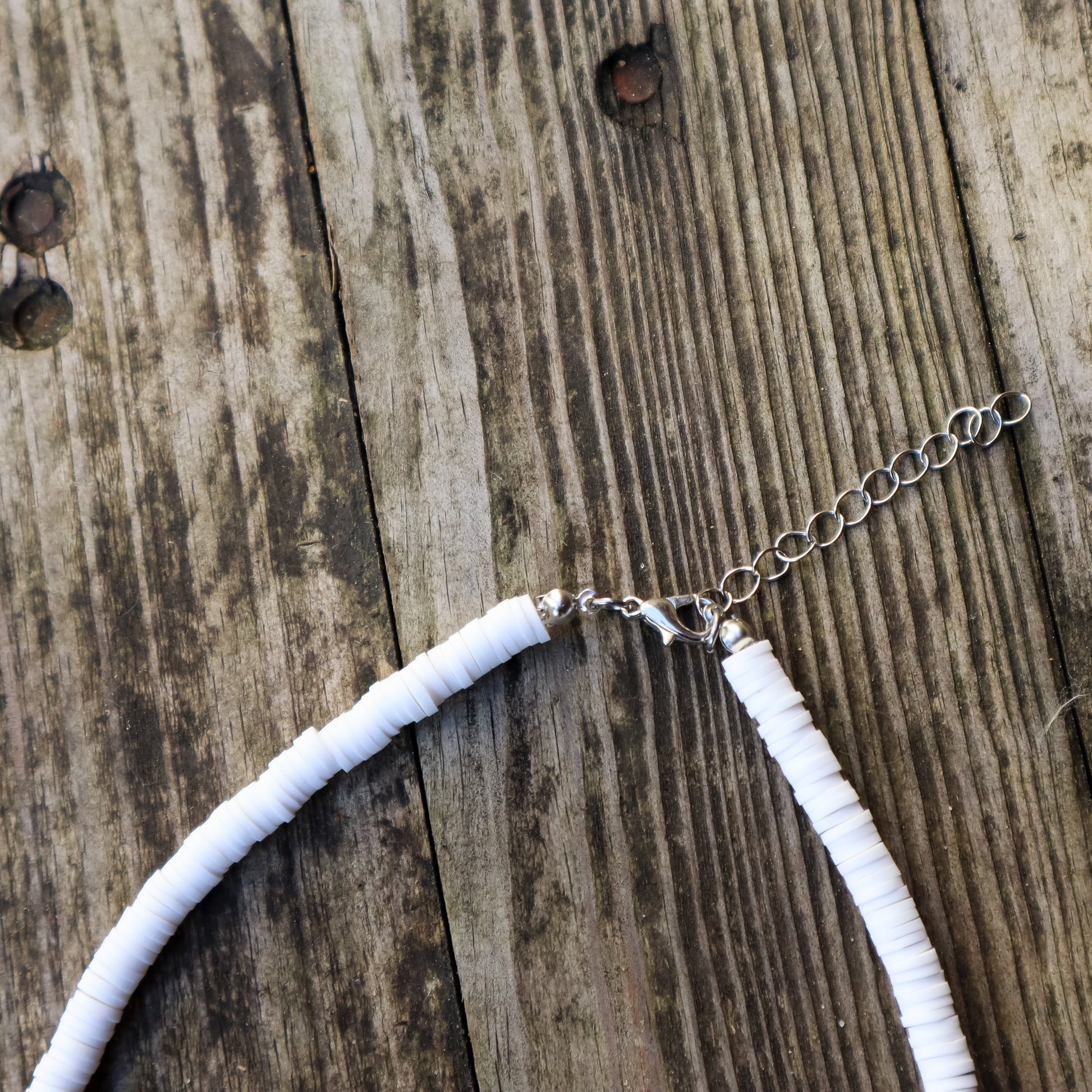 Necklace with white clay beads and a lobster clasp closure and chain on a wooden surface