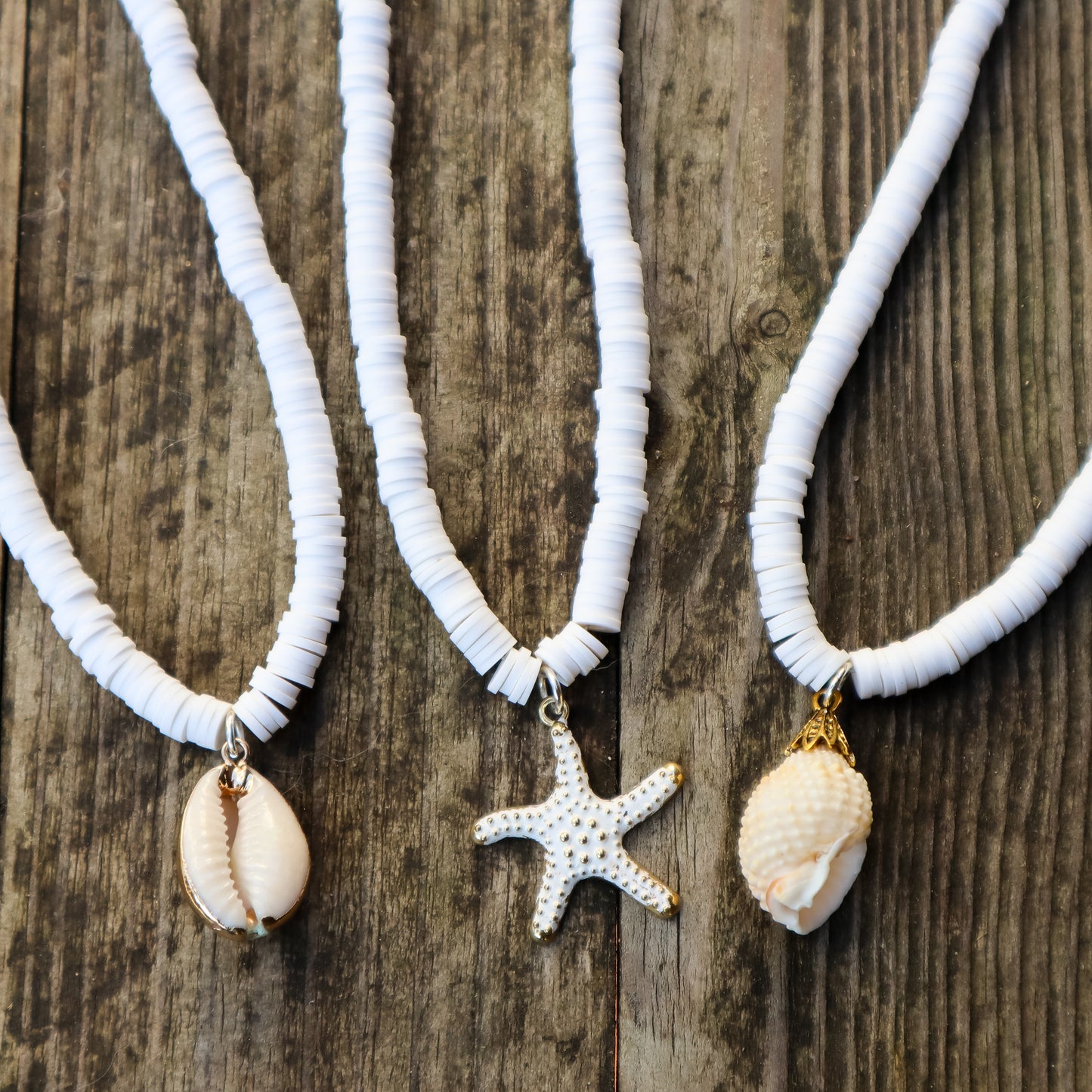 Three white beaded necklaces with shell and starfish pendants on a wooden surface