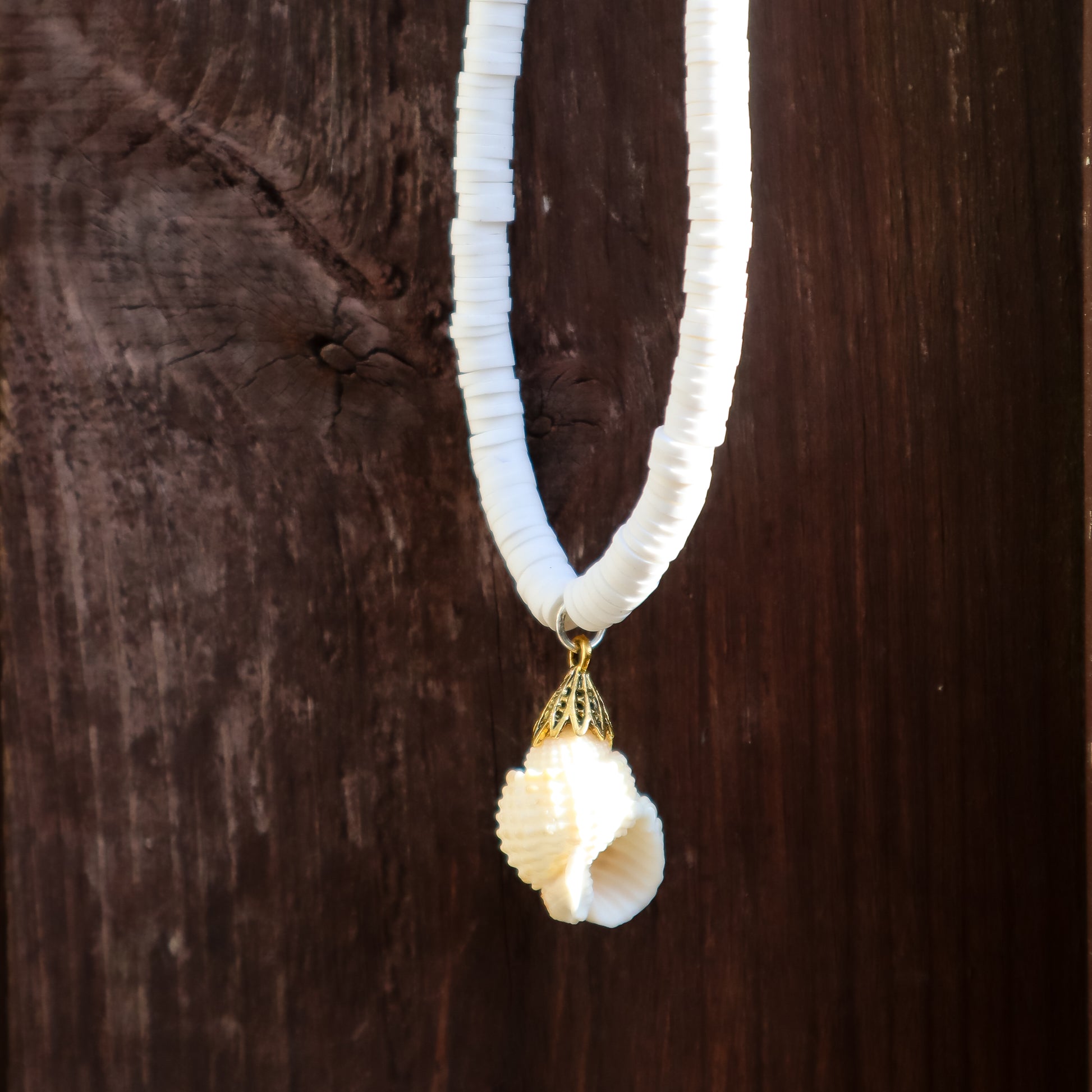 White beaded necklace with a shell pendant on a wooden background