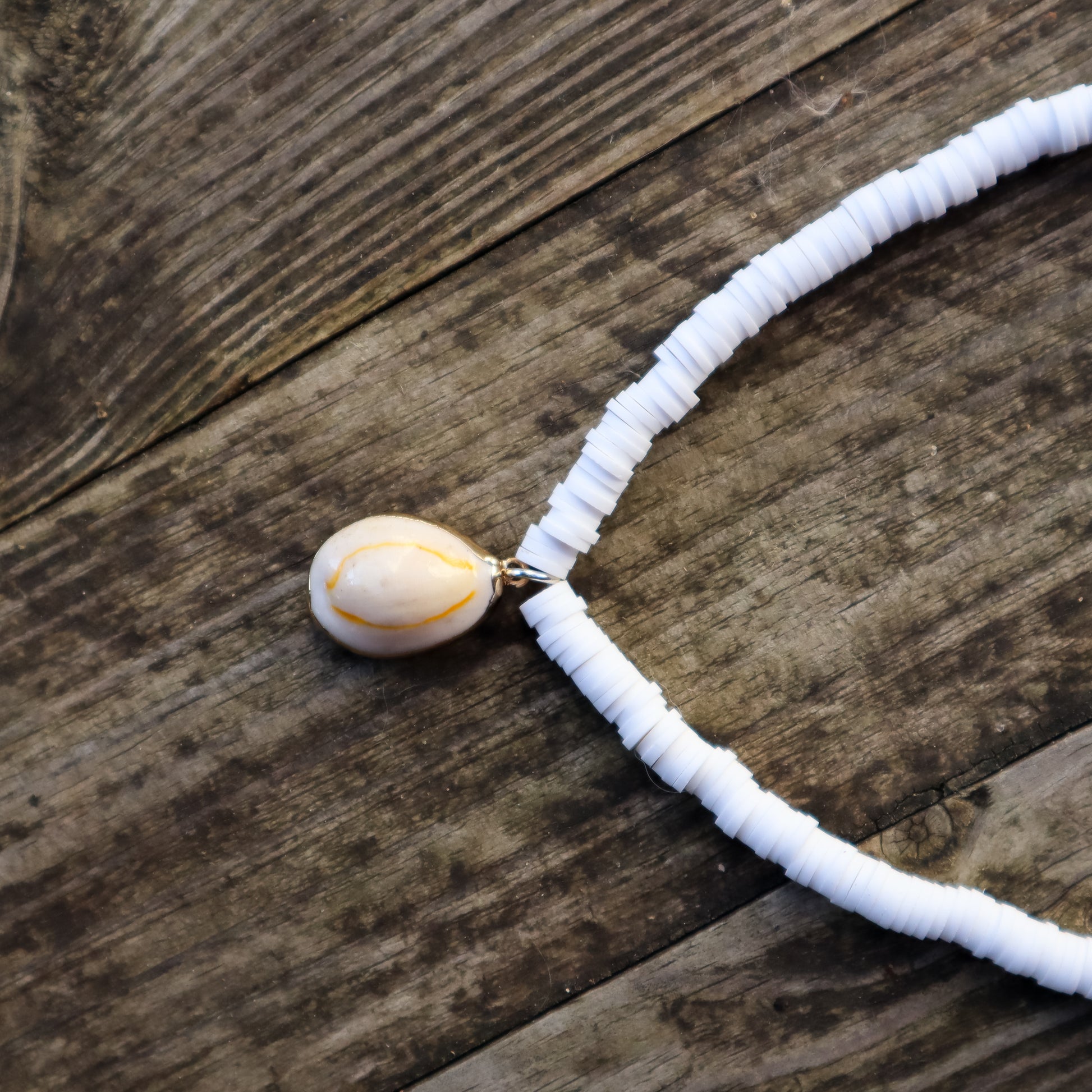 Necklace with a white beaded chain and a cowrie shell pendant on a wooden surface