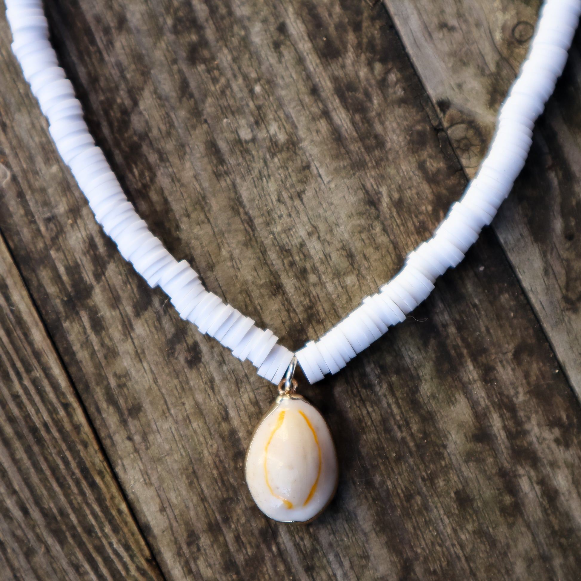 Necklace with white beads and a shell pendant on a wooden surface