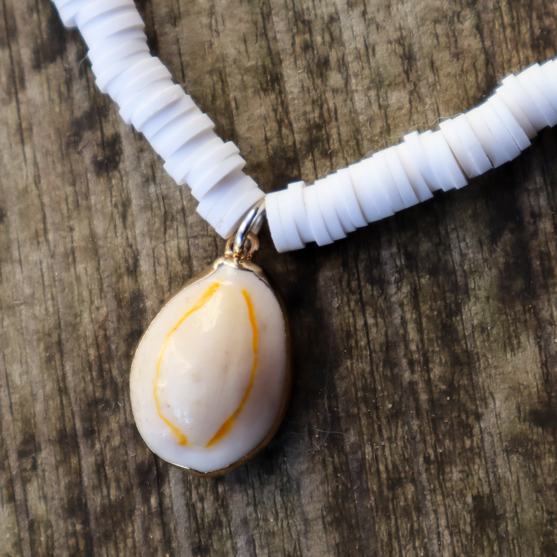 White necklace with white beads and a central cowrie shell pendant on a wooden surface