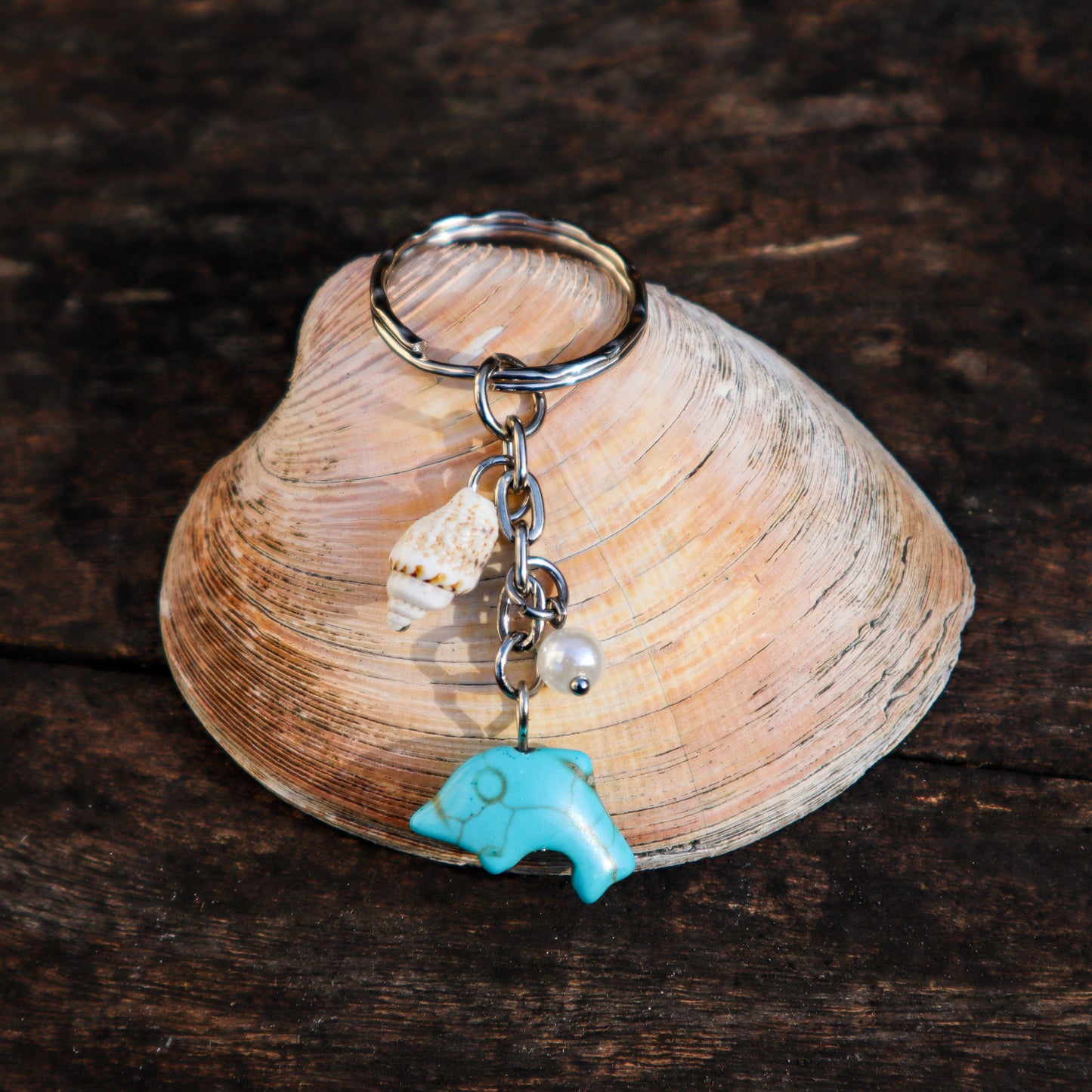 Keychain with a turquoise charm, pearl, and small shell on a seashell against a wooden background