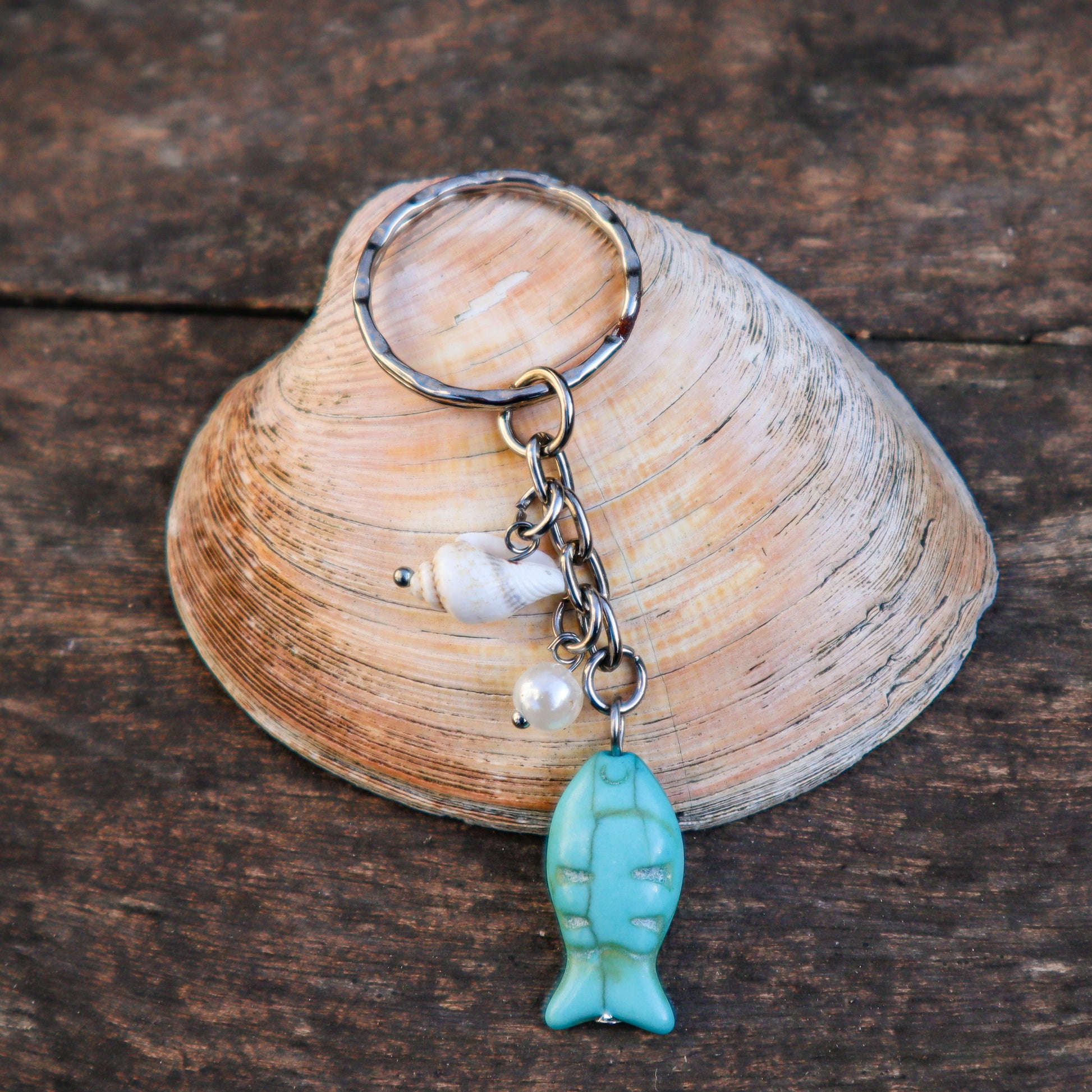 Keychain with fish charm on a shell against a wooden background