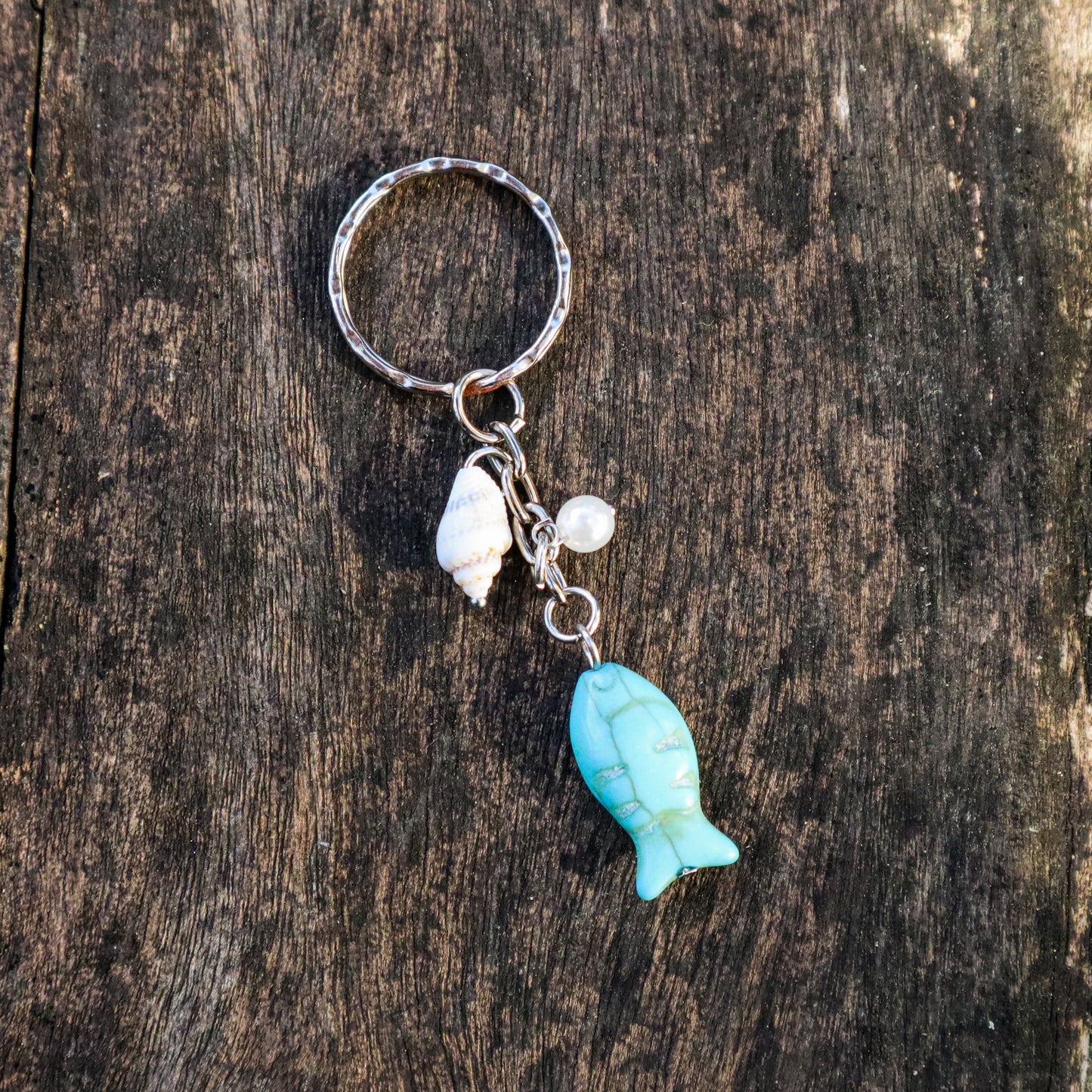 Keychain with turquoise fish charm and seashell on a wooden surface