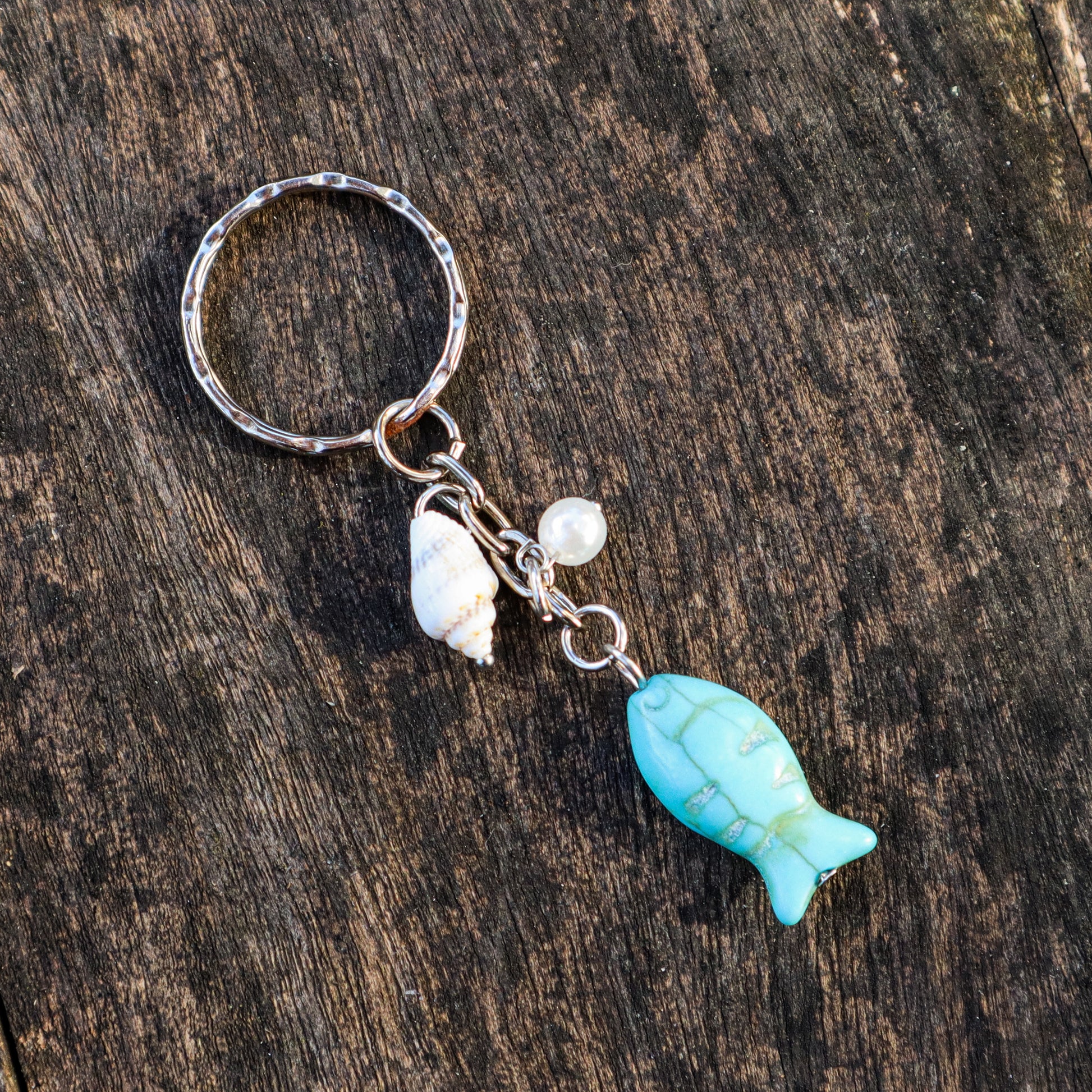 Keychain with turquoise fish charm and seashell on a wooden surface