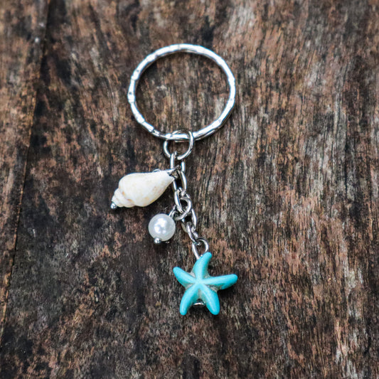 Keychain with starfish, shell, and pearl charm on a wooden surface